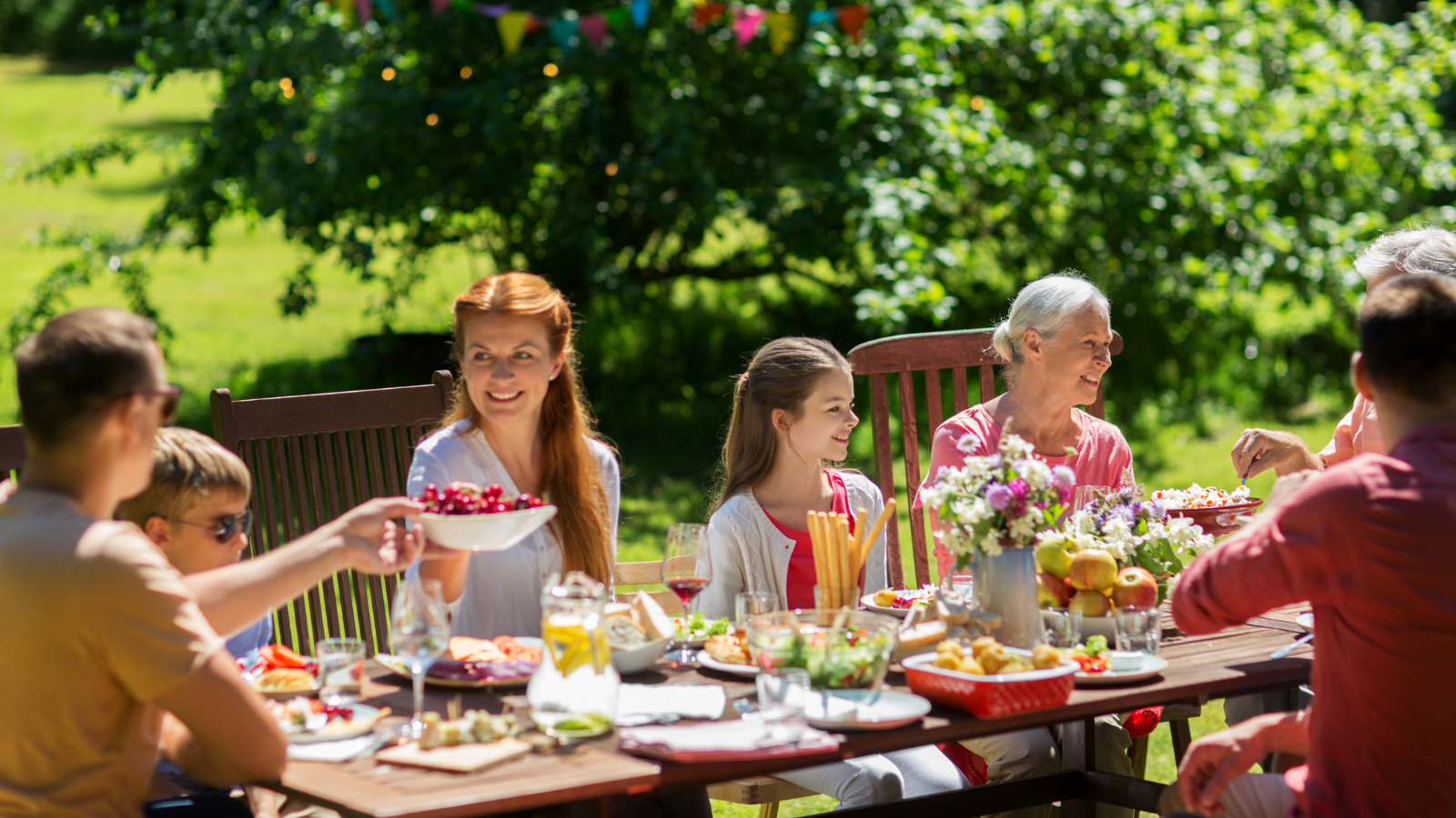 "A family gathering outdoors, enjoying a meal together at a beautifully set table in a garden