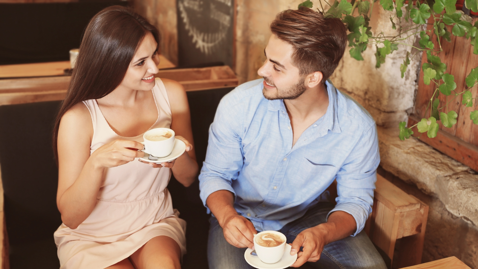 A couple enjoying coffee together at a cozy café, looking at each other and smiling warmly.