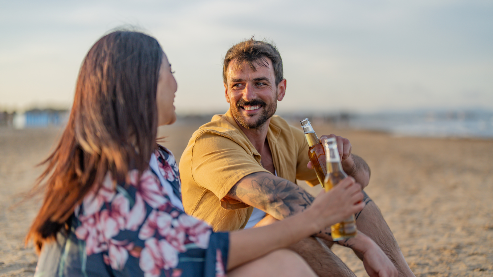 A couple chatting on the beach, smiling at each other and enjoying a relaxed moment.