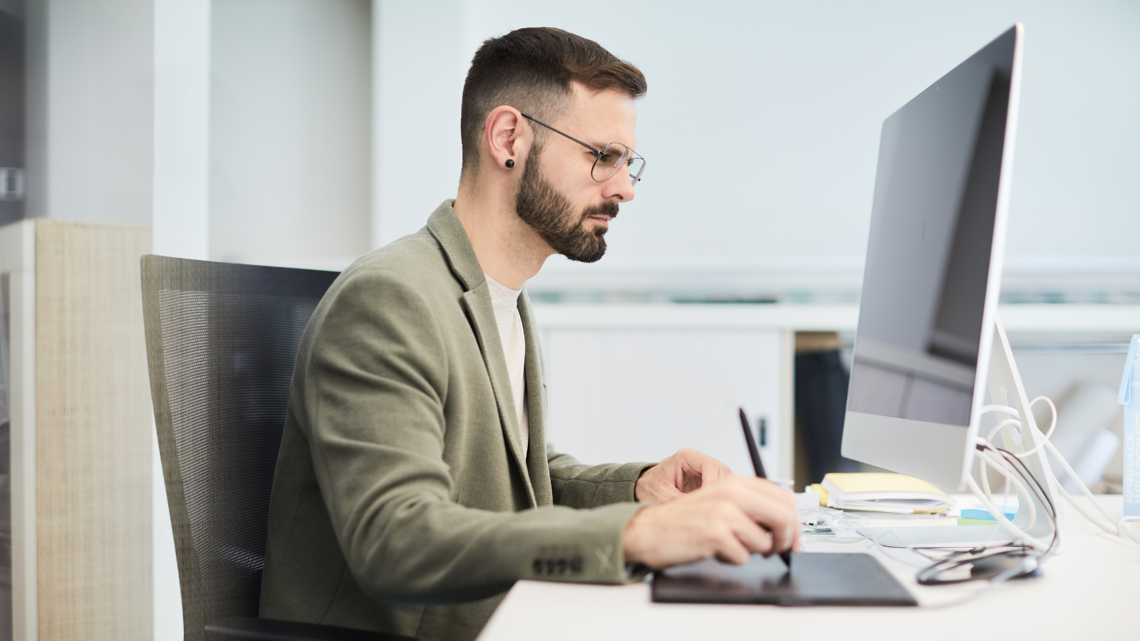 "A man working diligently at his desk with a computer and office supplies, focused on his task."