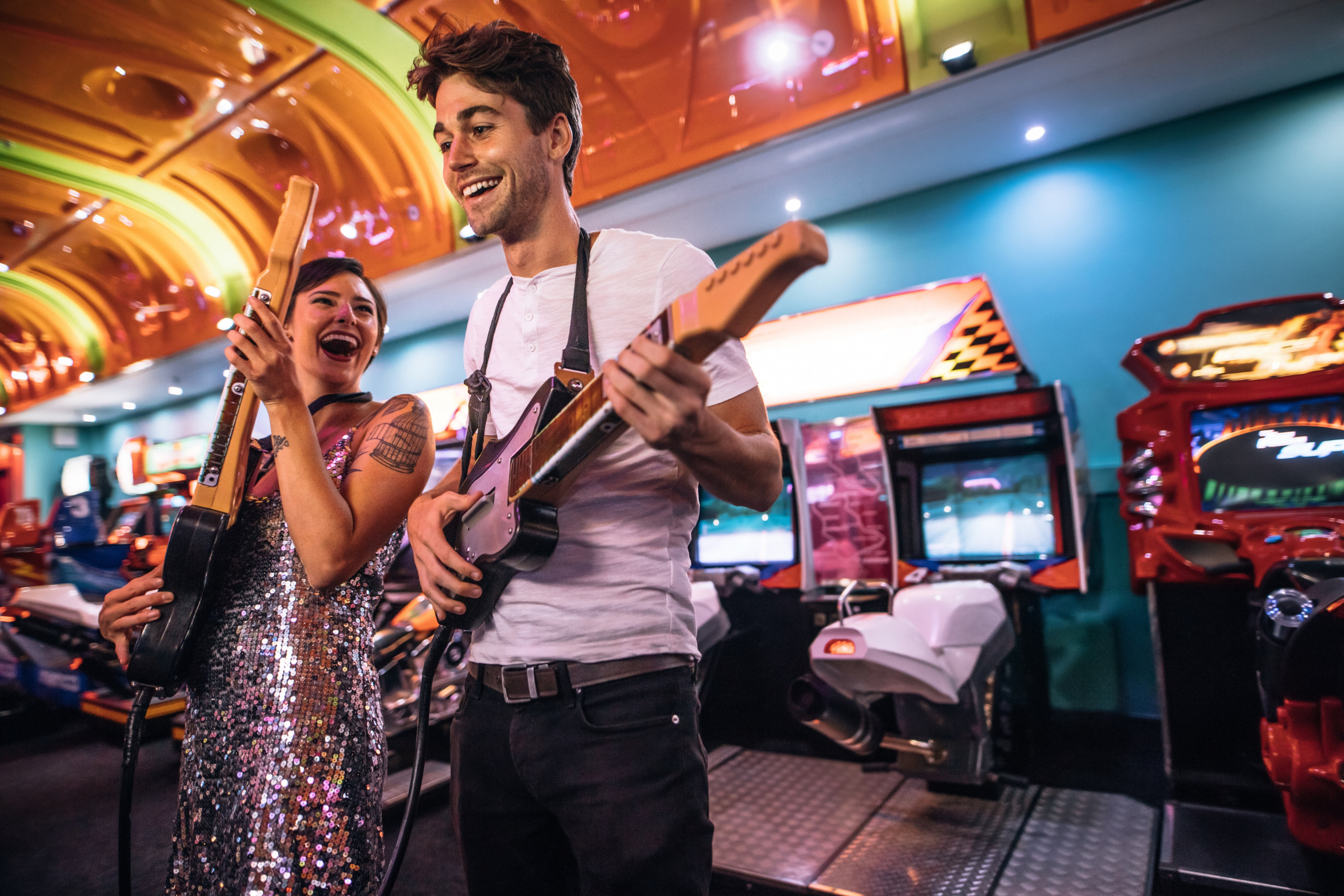 A young man and woman on a fun date at an arcade, playing a guitar game together. Their smiles and lively environment contrast with the concept of dating fatigue, showcasing the importance of enjoying the moment amidst the dating journey.