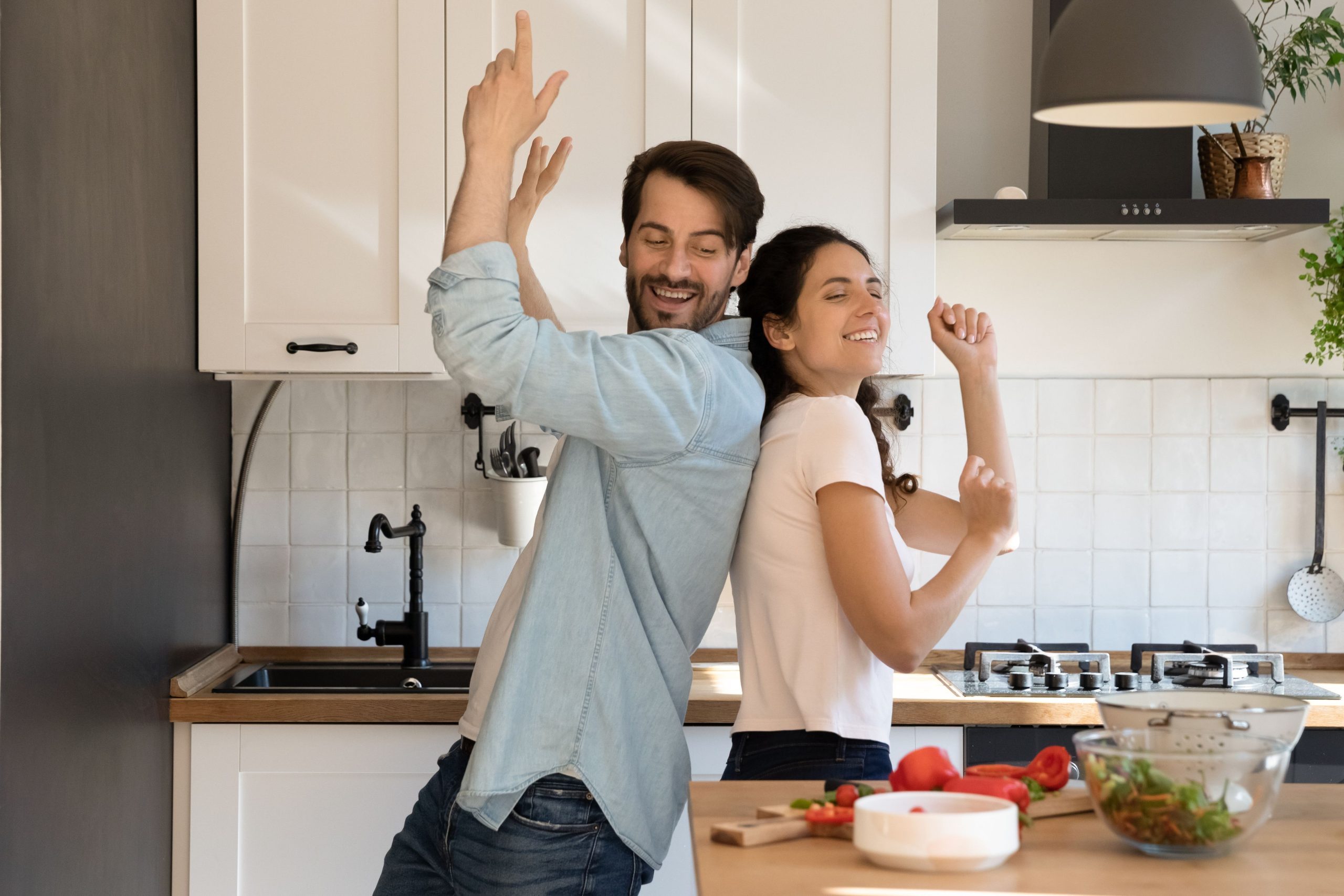 A couple dancing playfully in the kitchen while cooking, symbolizing a fun and intimate bond, with both smiling and enjoying the moment.