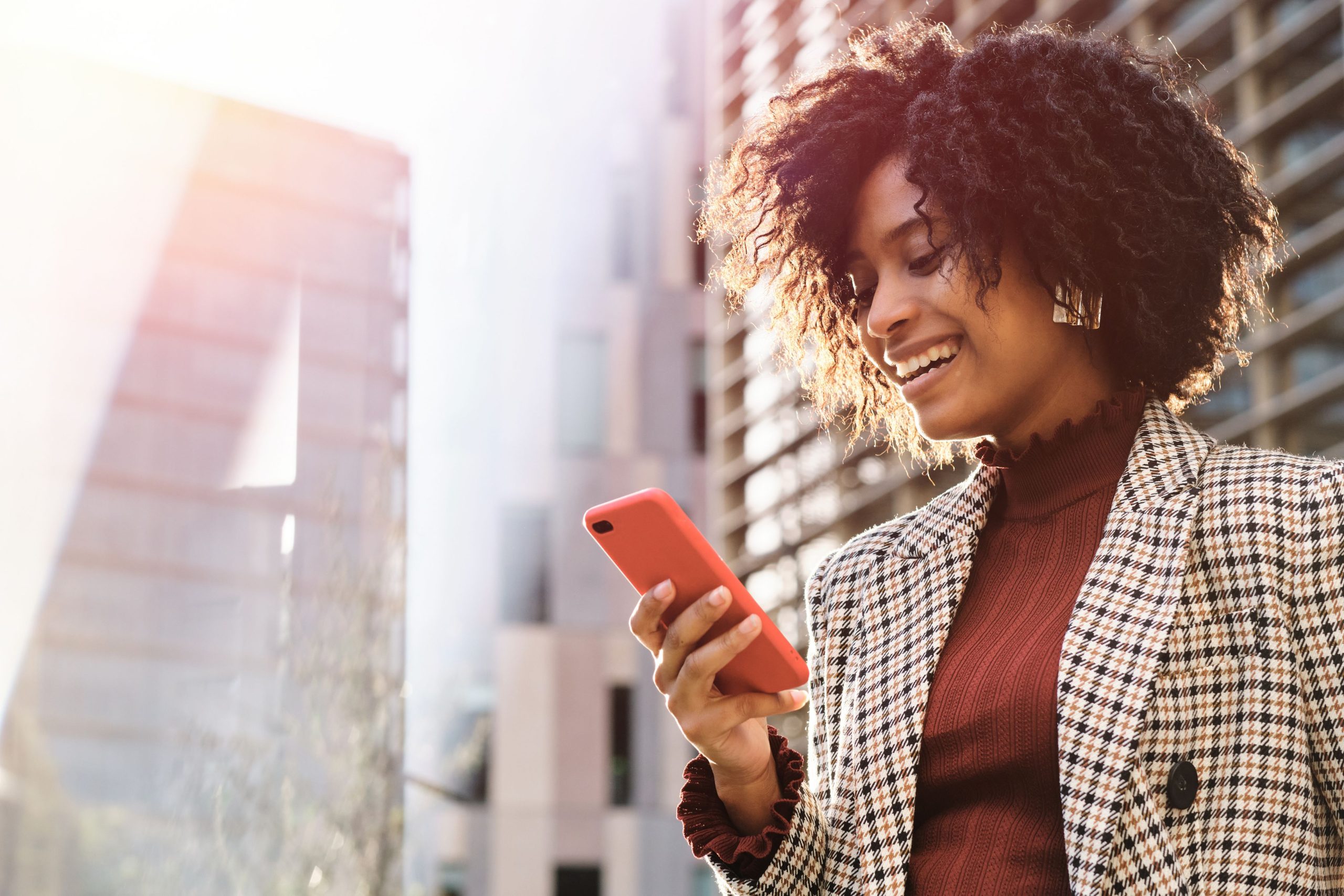 A woman smiling while looking at her phone, reflecting the positive and engaging experience of using humor in online dating conversations