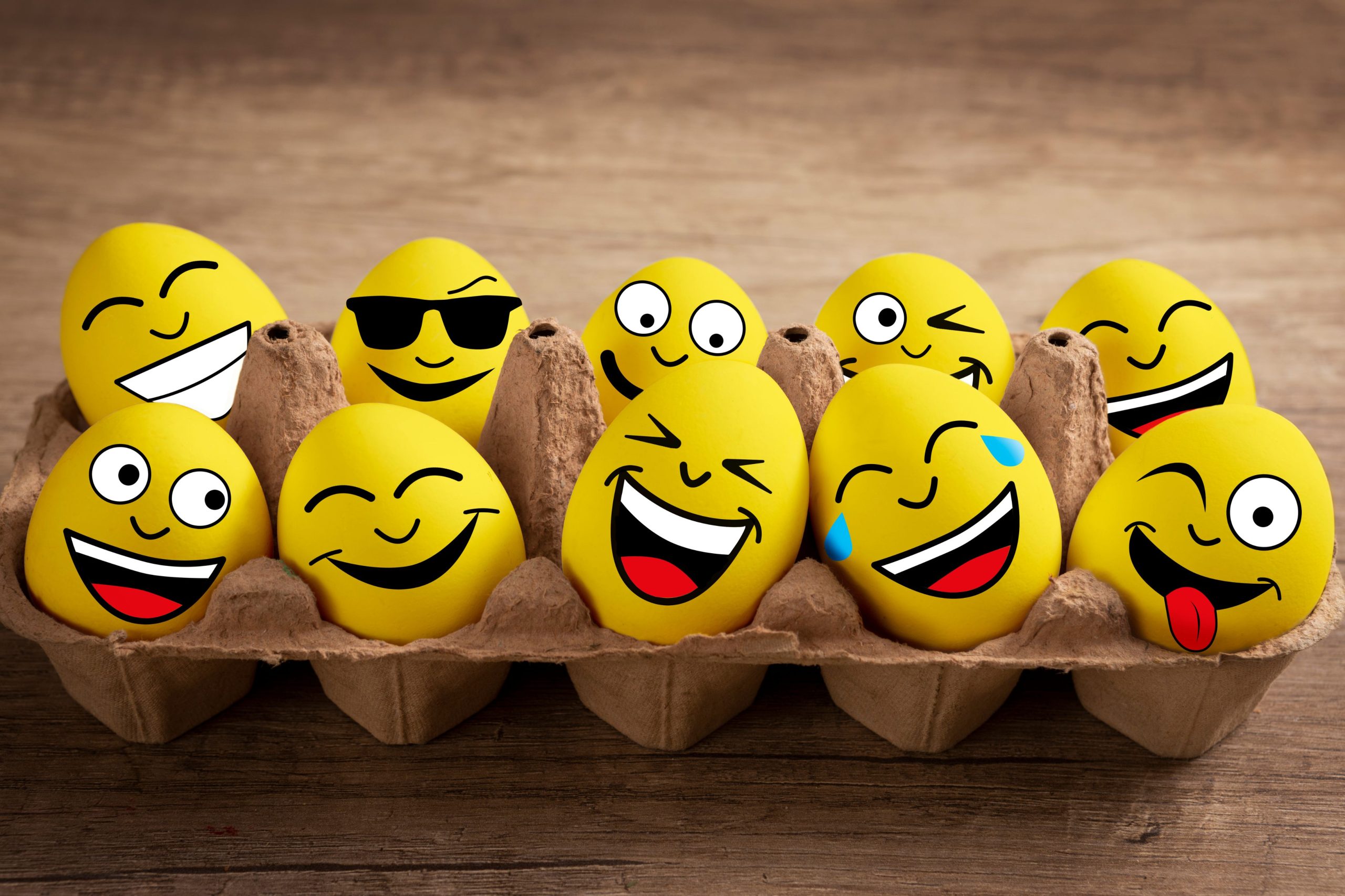 Carton of yellow eggs with drawn-on smiley faces, symbolizing different types of humor and their ability to lighten the mood in online dating interactions.